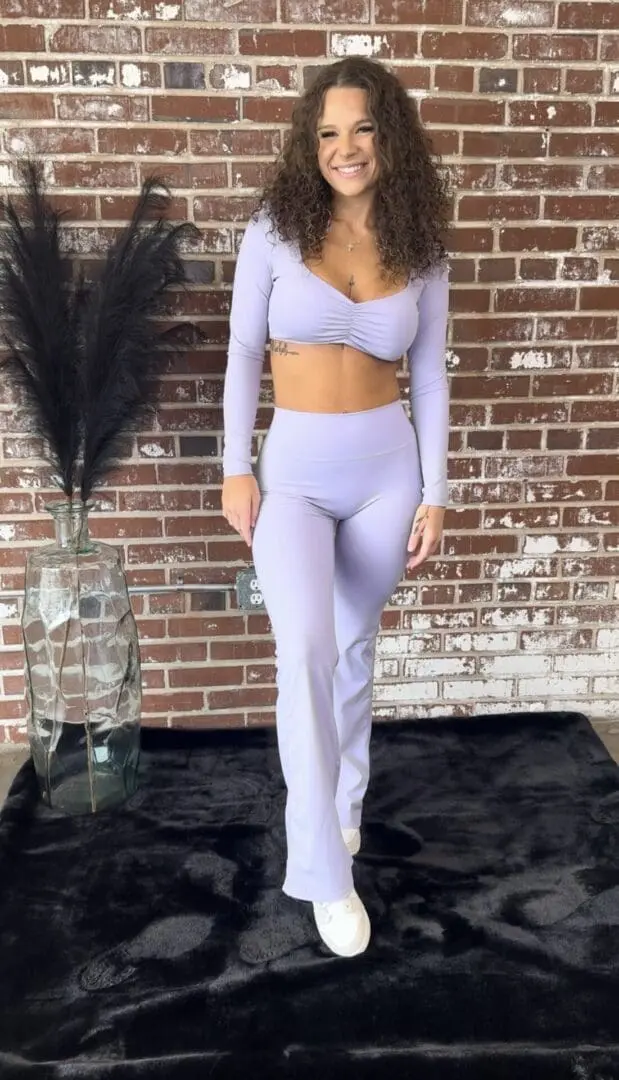 A woman in a lavender outfit standing next to a brick wall.